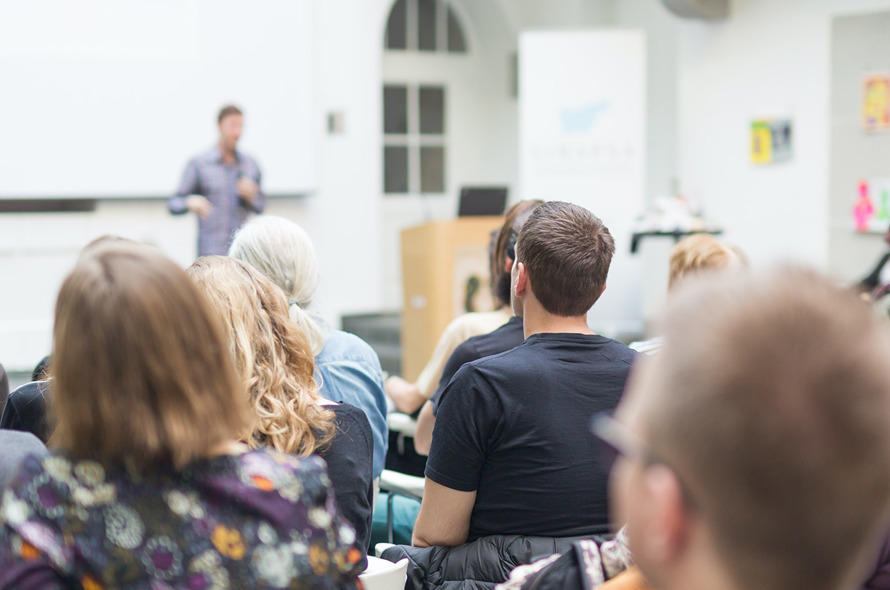 En gruppe mennesker sidder ved borde og ser op mod en underviser